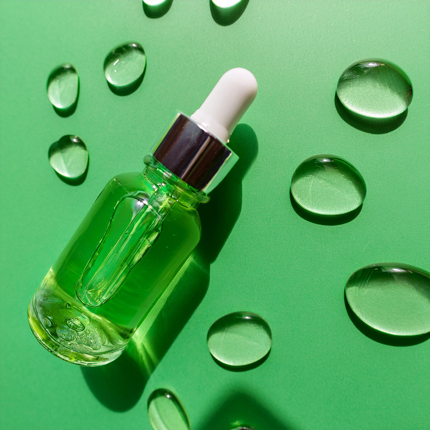 vista de un frasco de vidrio con cierre de bomba lleno de líquido transparente – sérum de ácido hialurónico. Alrededor del frasco con el sérum hay varias gotas de sérum derramado sobre el fondo. El fondo consiste en un fondo liso, verde claro. El frasco con el sérum está tumbado. Vista superior e iluminación de estudio