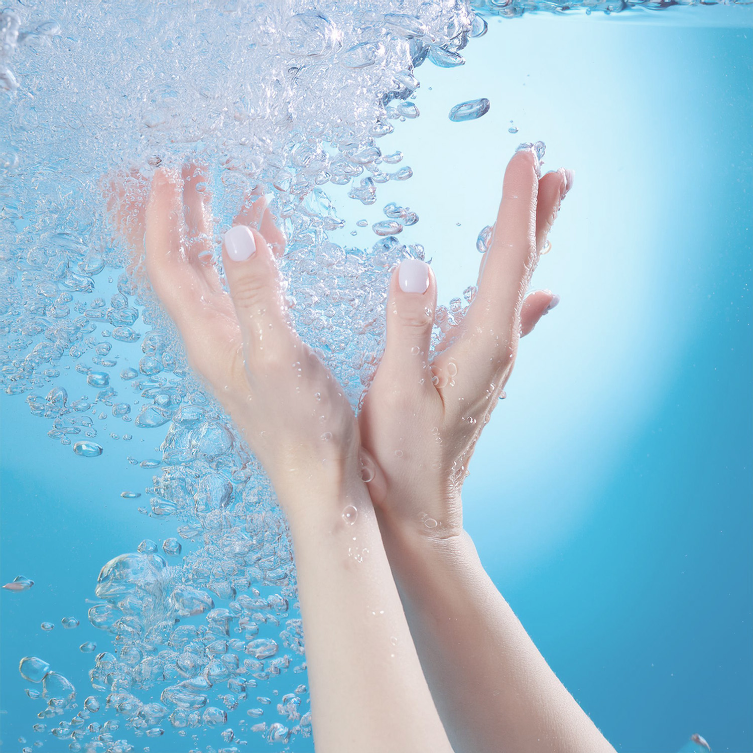 View of a woman’s hands in water, the whole photo has a pale blue tint and bubbles all around.