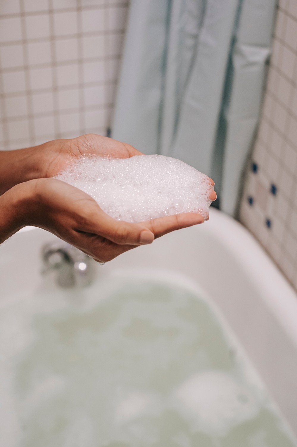 Hands holding foam full of surfactants in a bathroom space.